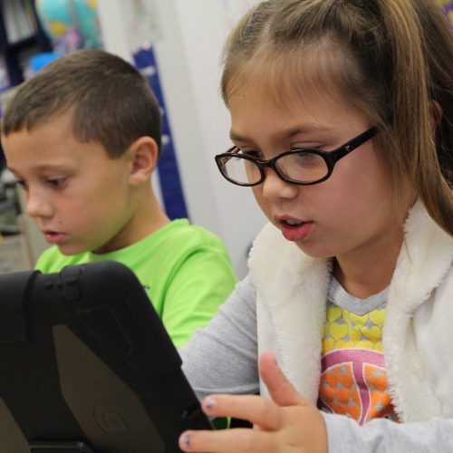 Two children using iPads in a classroom
